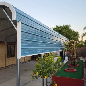 Residential blue and white metal carport protecting a driveway, next to a landscaped garden area with yellow flowers