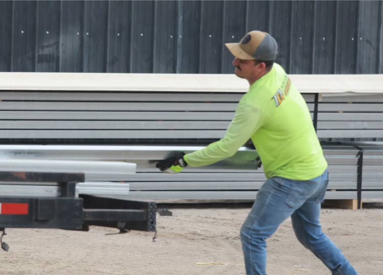Construction worker in neon shirt moving stacked metal building materials and framing on a dirt lot
