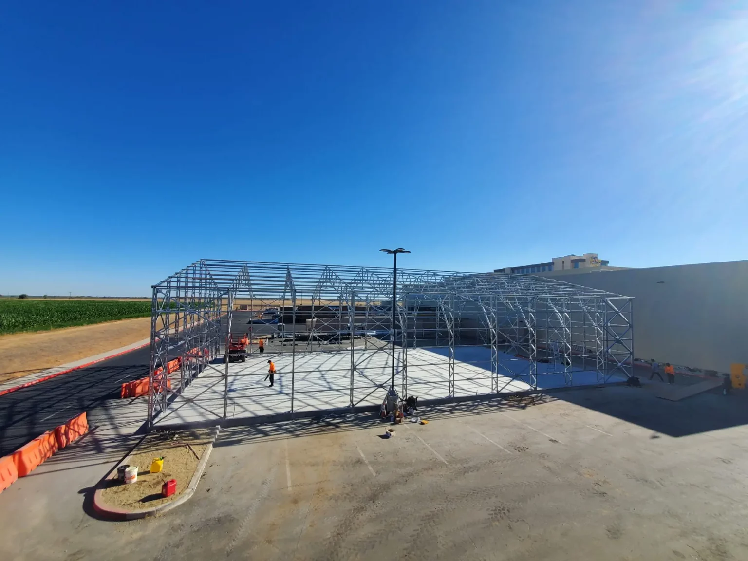 Construction worker in a bright green shirt unloading a large stack of galvanized steel beams or framing components from a trailer at a metal carports construction site