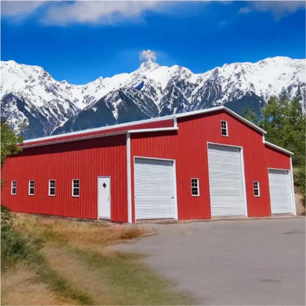 Large red metal building or barn with white trim and roll-up doors, set against a backdrop of snow-capped mountains