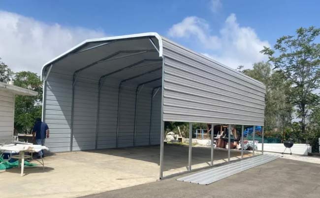Large grey metal carport with vertical roof style and partial side paneling installed on a concrete foundation for maximum vehicle protection.