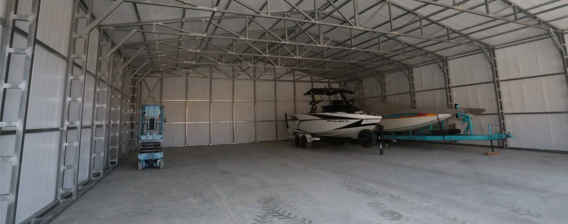 Large enclosed metal workshop building with three white roll-up doors and two-tone brown siding situated in a dense pine forest setting.